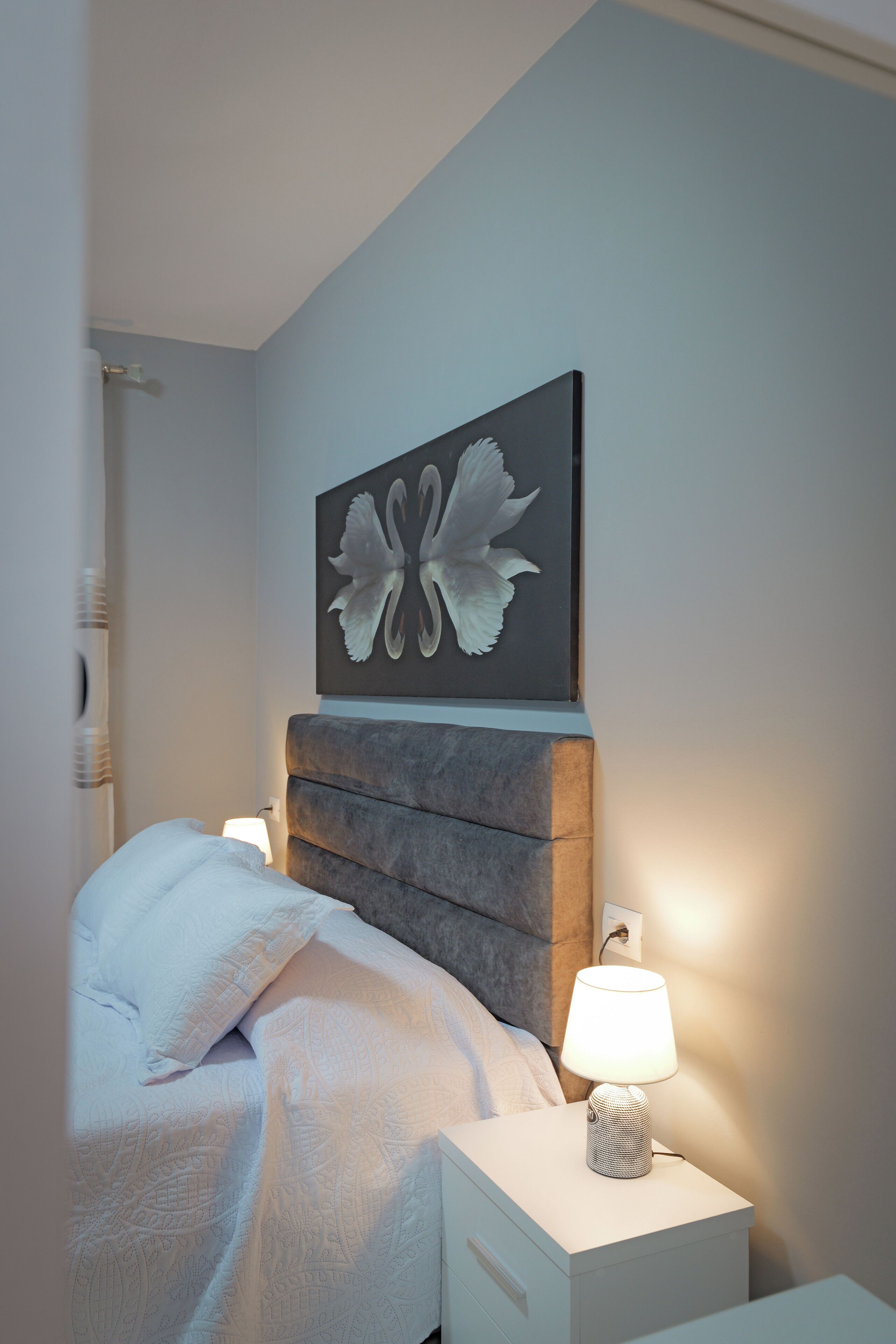 A bedroom with a bed, a bedside lamp, and a wall-mounted artwork.