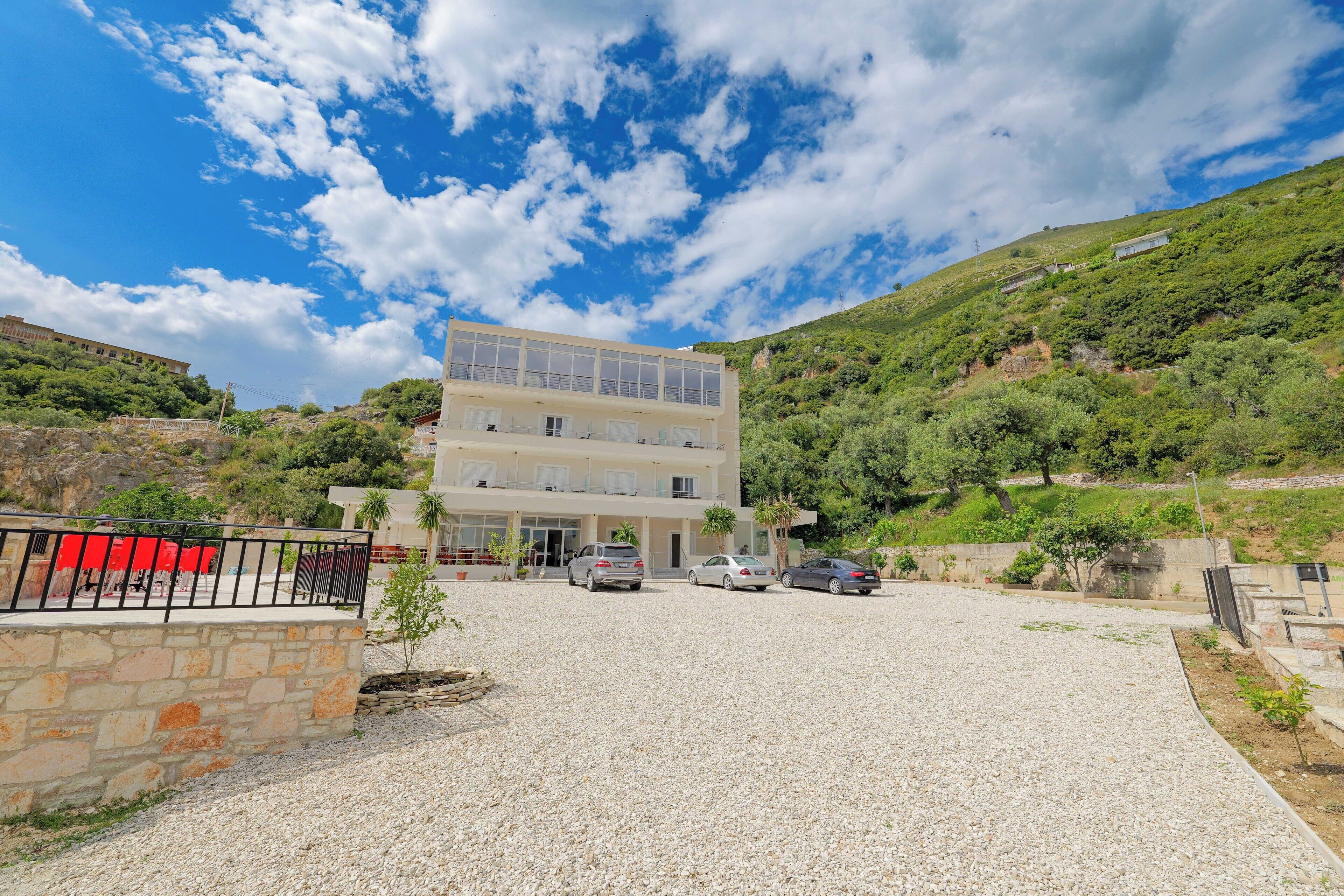 A multi-story building with a gravel driveway and parked cars.
