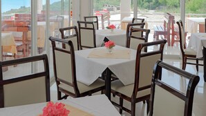 Un comedor con mesas y sillas, ventanas amplias con vistas al mar y al verdor.