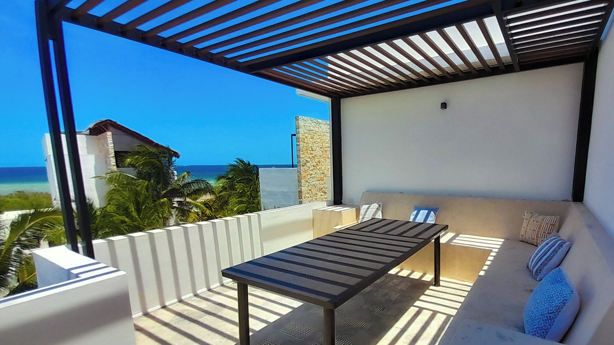 A balcony with a table and a sofa, overlooking a beach and ocean.
