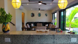 A modern living area with a sofa set, a coffee table, and a large window offering a view of greenery. - Corcomoran Luxury Beachfront house (Telchac Puerto)