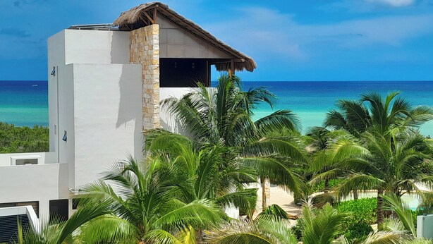 A modern building with a stone facade and a thatched roof, overlooking a beach with palm trees and the ocean. - Corcomoran Luxury Beachfront house (Telchac Puerto)