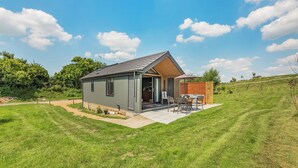 Een klein huis met een terras, een overdekte buiten zithoek en een gazon.