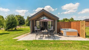 Een overdekt terras buiten met een jacuzzi, een tafel met stoelen en een houten omheining.