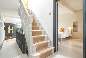 Staircase leads to a cozy upper level with a sofa, bedside table, and bookshelf.