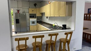 A kitchen with wooden cabinets, a stainless steel refrigerator, an oven, and a sink. There are three wooden stools in front of the counter. - Tahiti Diamond Rest Farm (Girardot)