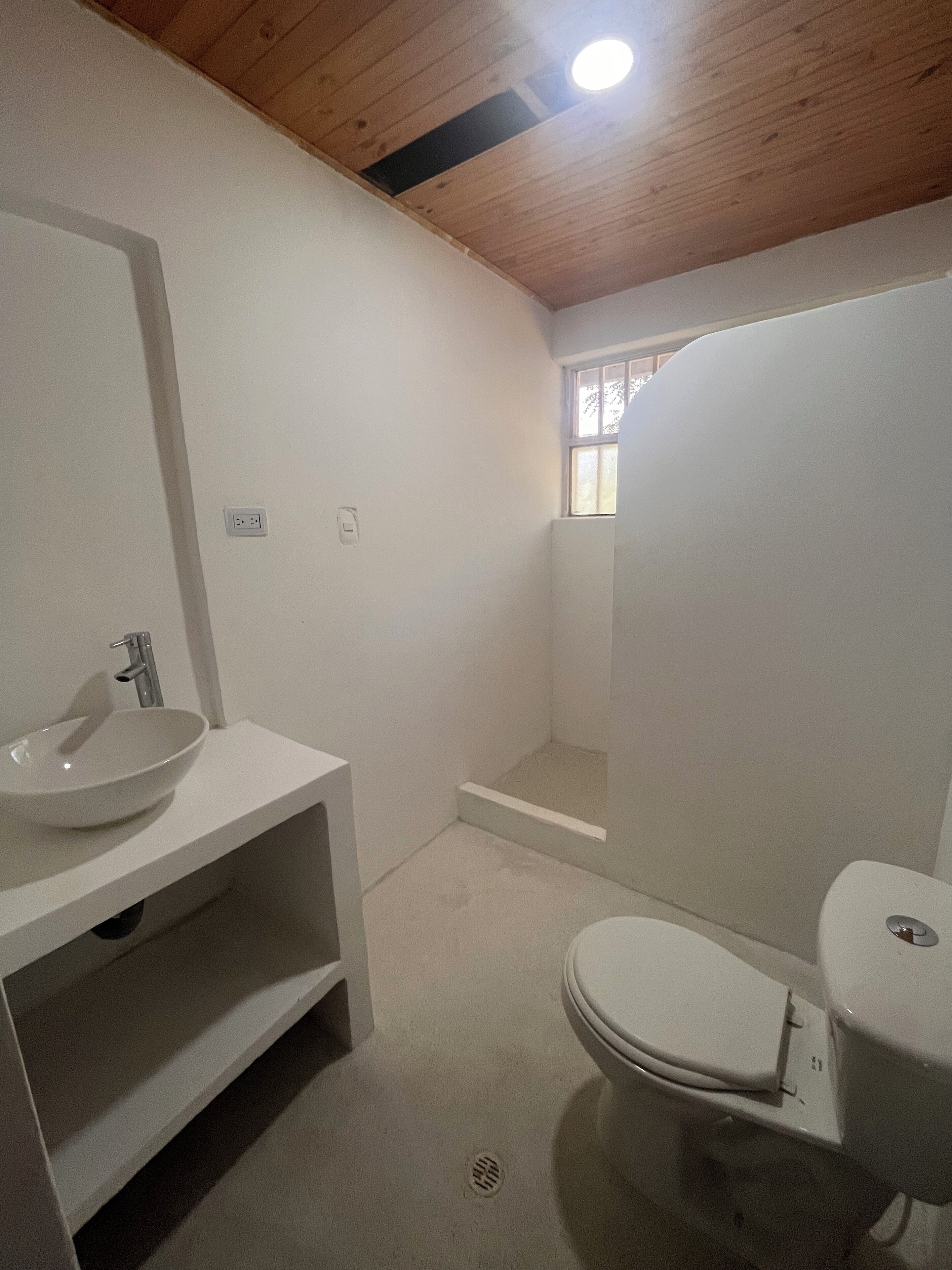Une petite salle de bain moderne avec un lavabo, des toilettes et une douche, le tout de couleur blanche.