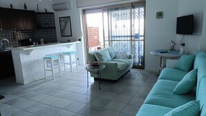 A modern living room with a teal sofa, a dining area with a kitchen island, and a sliding glass door leading to a balcony. - Margarita Ocean View Apartment (Sant'Alessio Siculo)