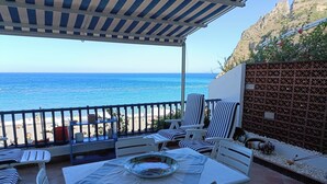 A terrace with a view of the sea, featuring striped chairs, a table with a bowl, and a covered area with a striped awning. - Margarita Ocean View Apartment (Sant'Alessio Siculo)