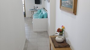 A hallway leading to a living area with a white sofa, a painting, and a small table with a bowl and flowers. - Margarita Ocean View Apartment (Sant'Alessio Siculo)