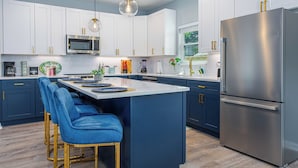 Une cuisine moderne avec des meubles blancs, un réfrigérateur en acier inoxydable et des tabourets de bar bleus.