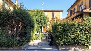 A narrow street with a yellow building, a motorcycle, and dense greenery. - Barbieri23 Design by Wonderful Italy (Bologna)