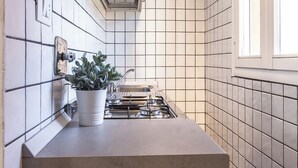A kitchen with white tiled walls, a gas stove, a potted plant, and a window. - Barbieri23 Design by Wonderful Italy (Bologna)