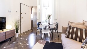 A modern living room with a sofa, a dining table with chairs, a TV on a wooden cabinet, and a potted plant. - Barbieri23 Design by Wonderful Italy (Bologna)