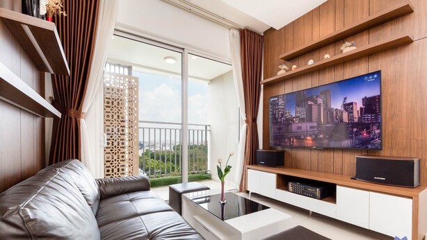 Una sala de estar moderna con un sofá de cuero, un televisor de pantalla plana montado en una pared de madera y un balcón con vista a la ciudad.