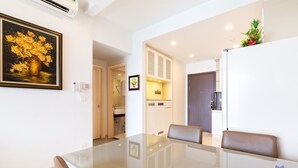 Una sala moderna con una mesa de comedor de vidrio, sillas de cuero, un cuadro de flores y una cocina visible a través de una puerta abierta.