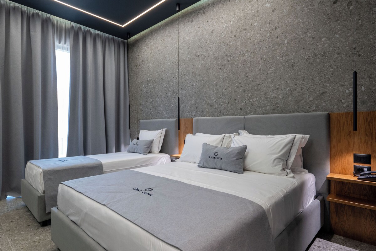 A modern hotel room with two beds, grey bedding, and a concrete accent wall.