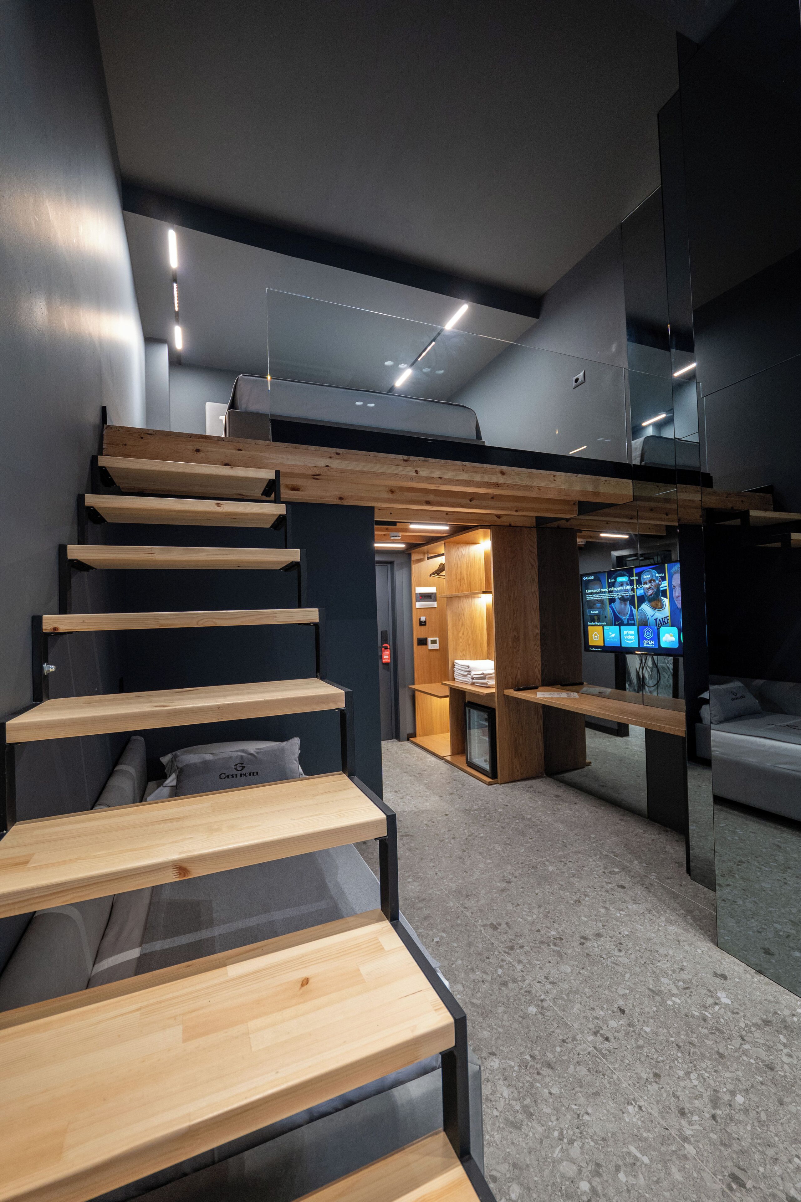 Un interno moderno con una scala in legno, una zona salotto e uno schermo televisivo.