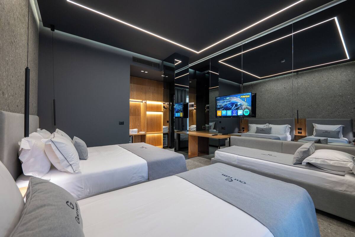 A modern hotel room with two single beds, a desk, and a TV.