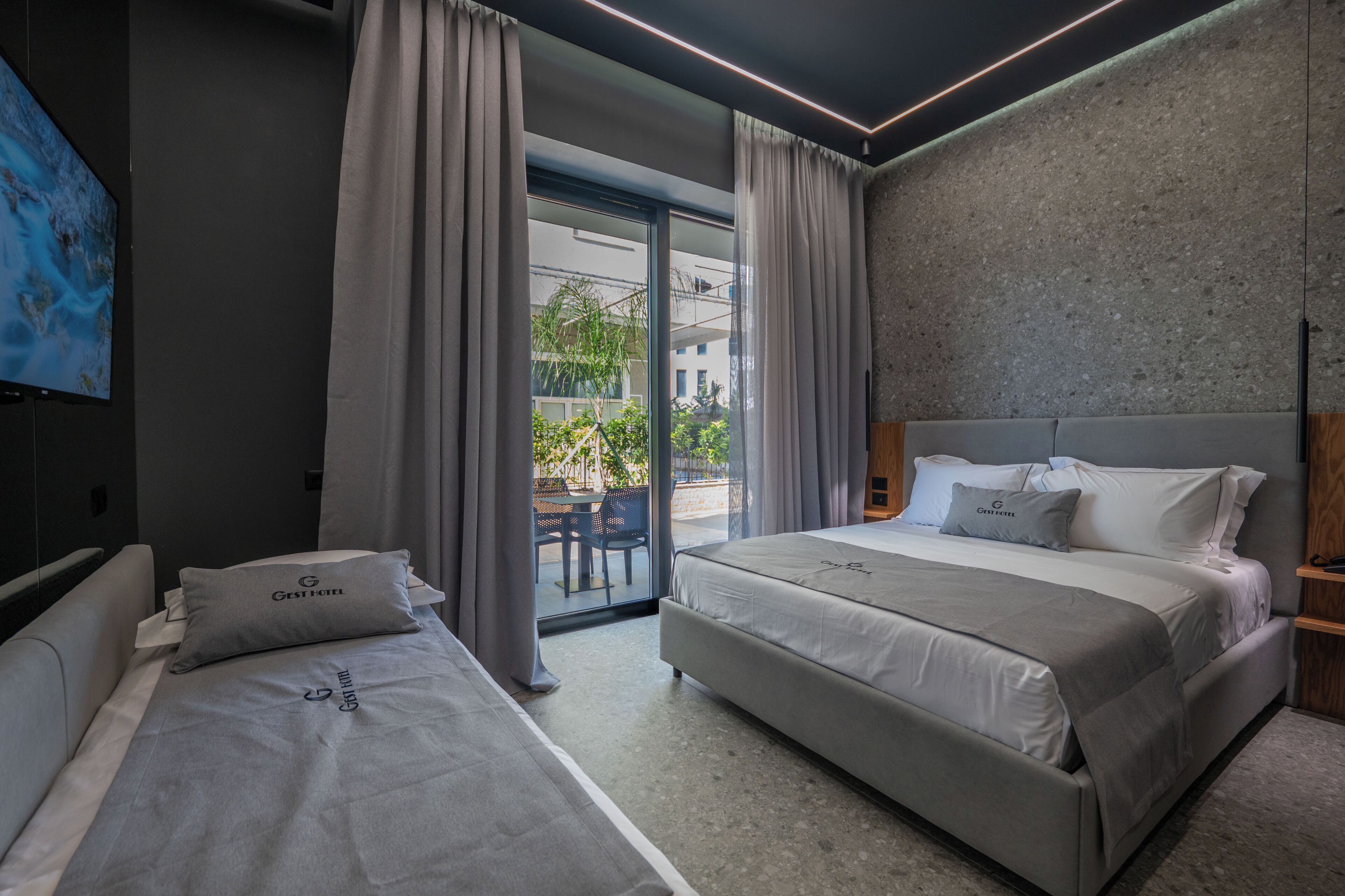 A modern hotel room with two beds, a large window, and a view of the outside.