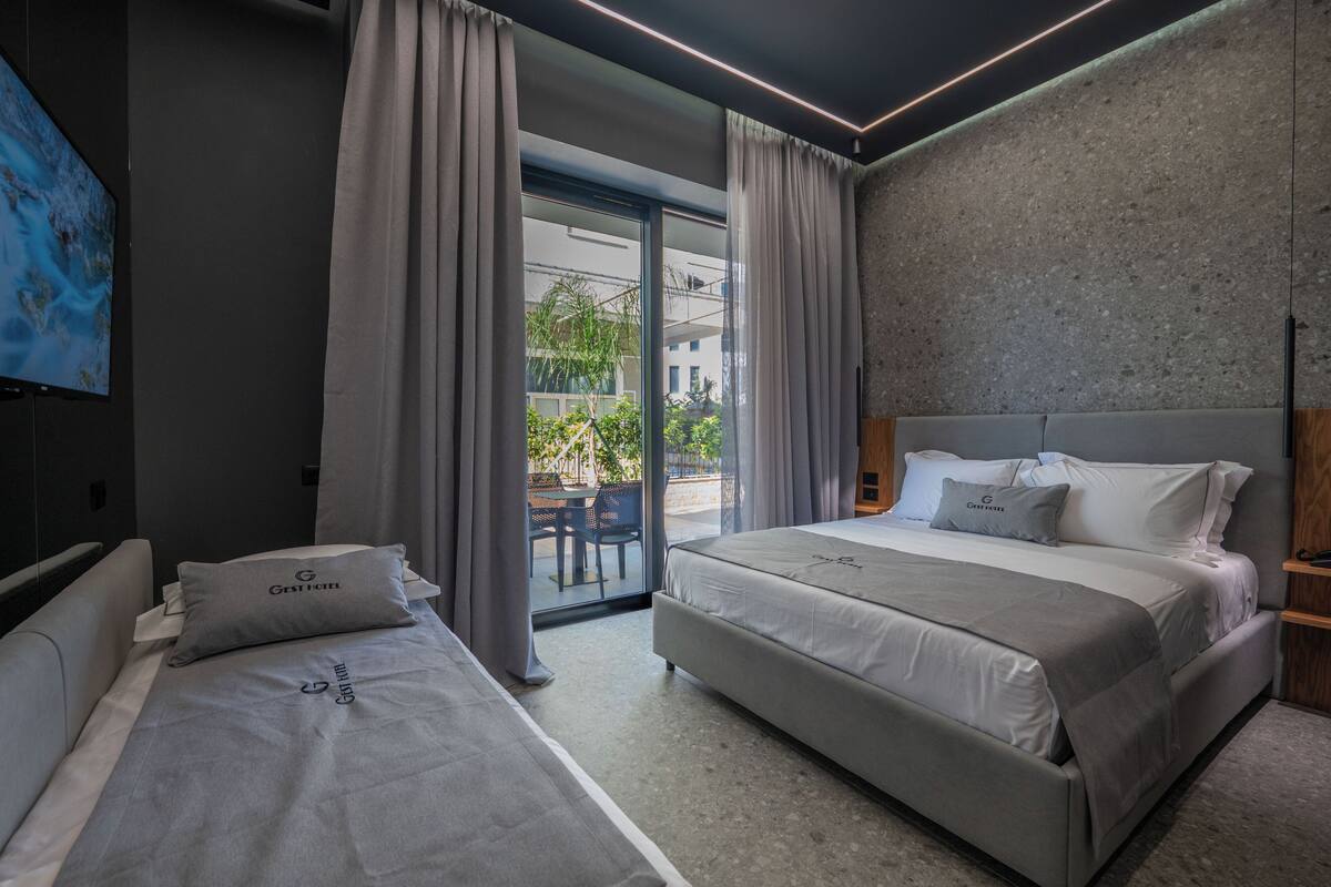 A modern hotel room with two beds, a large window, and a view of the outside.