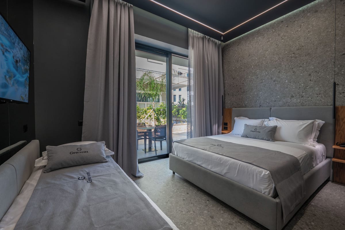 A modern hotel room with two beds, a large window, and a view of the outside.