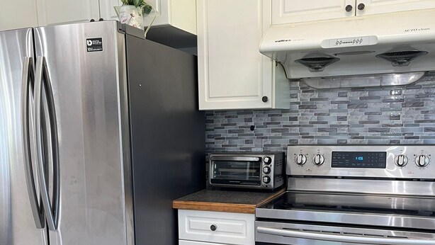 A modern kitchen with stainless steel appliances, white cabinetry, and a tiled backsplash.