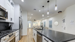 Una cocina moderna con armarios blancos, encimera negra, electrodomésticos de acero inoxidable e iluminación colgante.