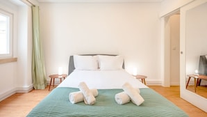 A neatly made bed with white linens and two rolled towels, a green textured blanket, and two bedside tables with candles. - GuestReady - Bright escape near Santa Apolónia (Lisbon)