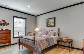 Une chambre à coucher avec un lit en bois, une commode, une table de chevet, une lampe et une fenêtre avec des stores.