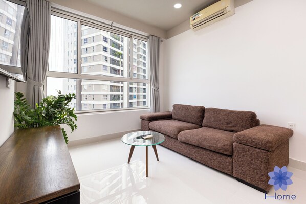 A living room with a brown sofa, a glass coffee table, a wooden side table, and a potted plant.