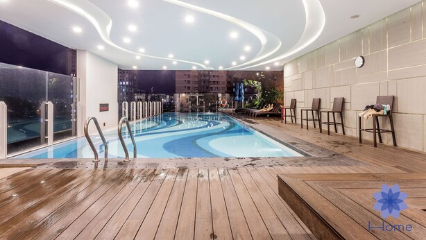 Una piscina interior con terraza de madera, rodeada de sillones de descanso y un diseño de techo moderno.
