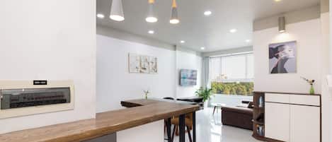 A modern kitchen with a wooden countertop, bar stools, pendant lights, and a built-in oven.