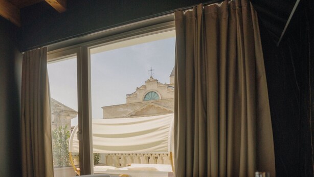 A hot tub with a view of a building with a dome and cross, curtains, and wooden beams. - Cinquanta Sfumature B&b Luxury Suites (Cassano delle Murge)