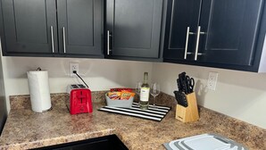 A kitchen with dark cabinets, a red toaster, a paper towel holder, a snack basket, a wine bottle, glasses, and a knife block. - Hot Stuff! Pro Cleaned Self Check In Sleeps 10 (Racine)