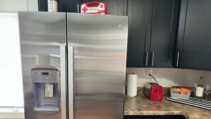 A stainless steel refrigerator with a water dispenser, a red toaster, a bottle of wine, and a bowl of chips on the kitchen counter. - Hot Stuff! Pro Cleaned Self Check In Sleeps 10 (Racine)