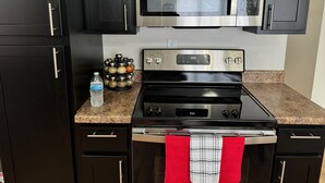 A kitchen with dark cabinets, a stainless steel microwave, a gas stove, and a water bottle on the counter. - Hot Stuff! Pro Cleaned Self Check In Sleeps 10 (Racine)