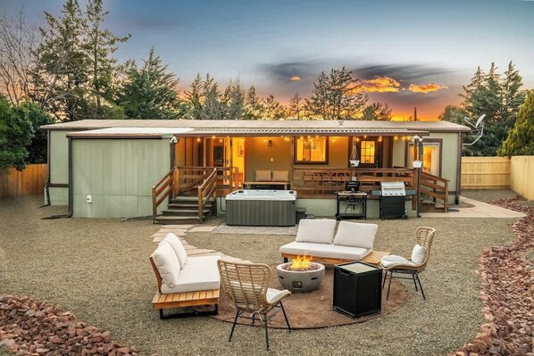 Ein Haus mit überdachter Terrasse, Sitzgelegenheiten im Freien, Whirlpool und Grillplatz.