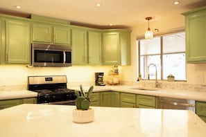Une cuisine avec des meubles de couleur verte, un four à micro-ondes en acier inoxydable, une cuisinière et une grande fenêtre donnant sur un beau paysage.