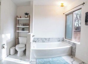 Ein modernes Badezimmer mit einer weißen Badewanne, einer Toilette und einem Pflanzenregal.