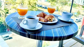 Ein Frühstückstisch mit Croissants, Kaffee und Orangensaft, mit Blick auf das Meer und die Stadt.