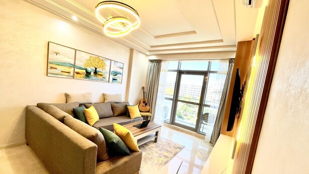 Ein modernes Wohnzimmer mit einem Ecksofa, einem Flachbildfernseher und einem großen Fenster mit Blick ins Freie.