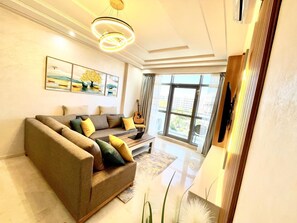 A modern living room with a sectional sofa, a flat-screen TV, and a large window offering a view of the outdoors. - Modern Tangier centre elegance with Seaview - Steps to Beach, train, attractions (Tangier)