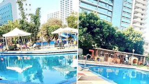 Ein Schwimmbad mit Liegestühlen und Sonnenschirmen, umgeben von Gebäuden und Bäumen.