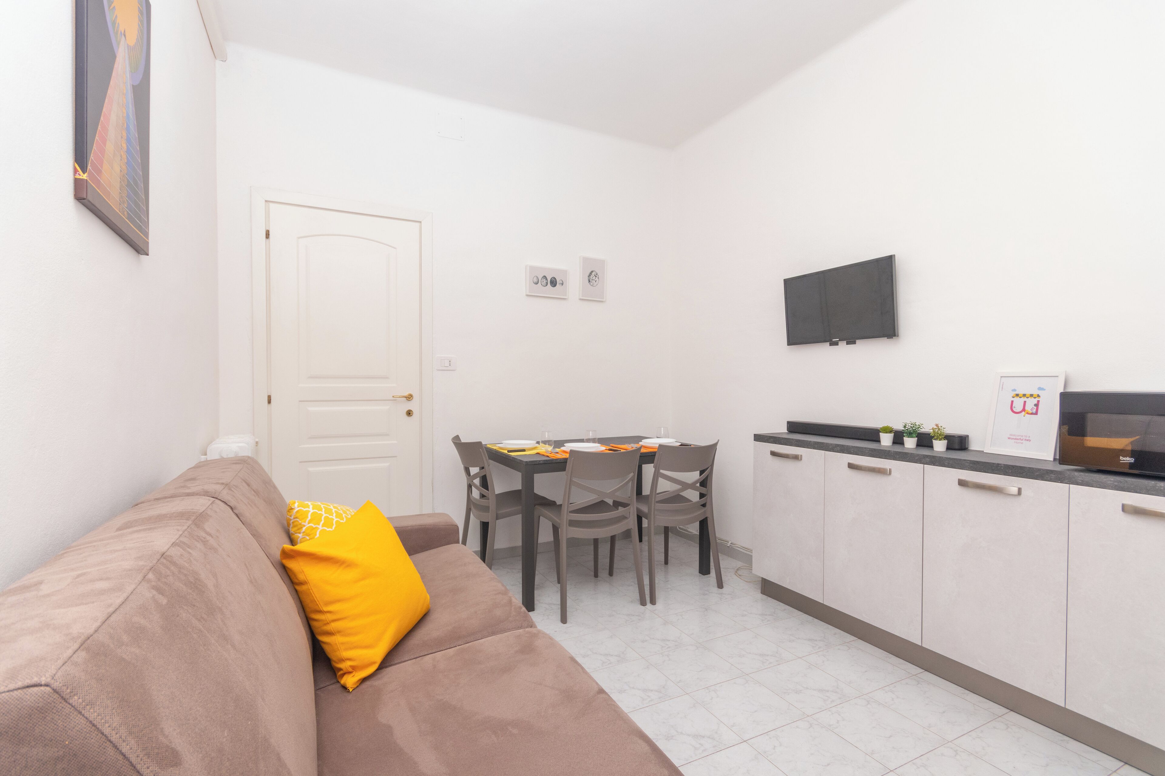 Un espacio habitable compacto con kitchenette, zona de comedor y sofá con cojín amarillo.