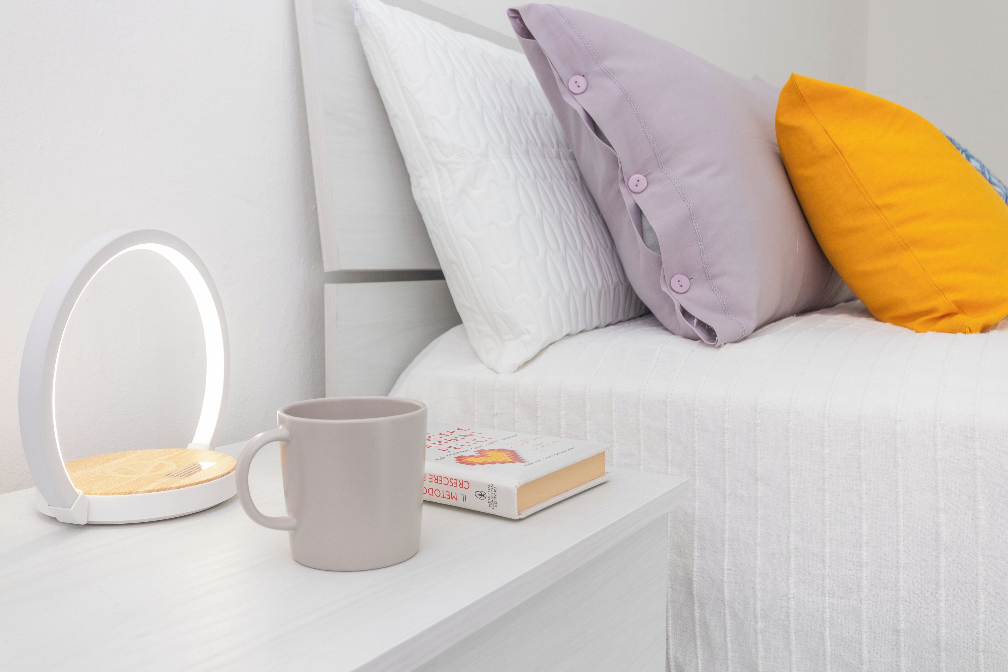 A neatly arranged bedside table with a book, a mug, and a white bedside lamp.