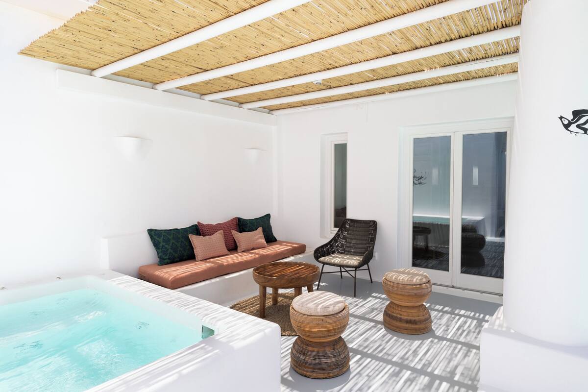 A modern outdoor lounge area with a hot tub, seating, and a view of the sea.