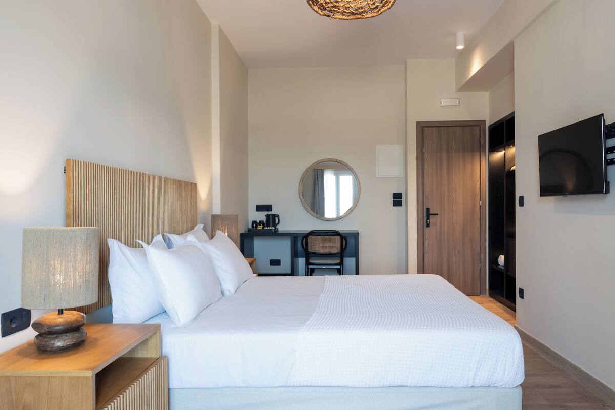 A modern hotel room with a large bed, a desk with a chair, a television, and a wardrobe.