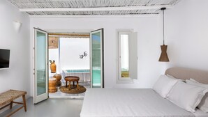 A bedroom with a bed, a bench, a TV, and a balcony with a view. - Casa Frati Suites & Villas (Santorini)