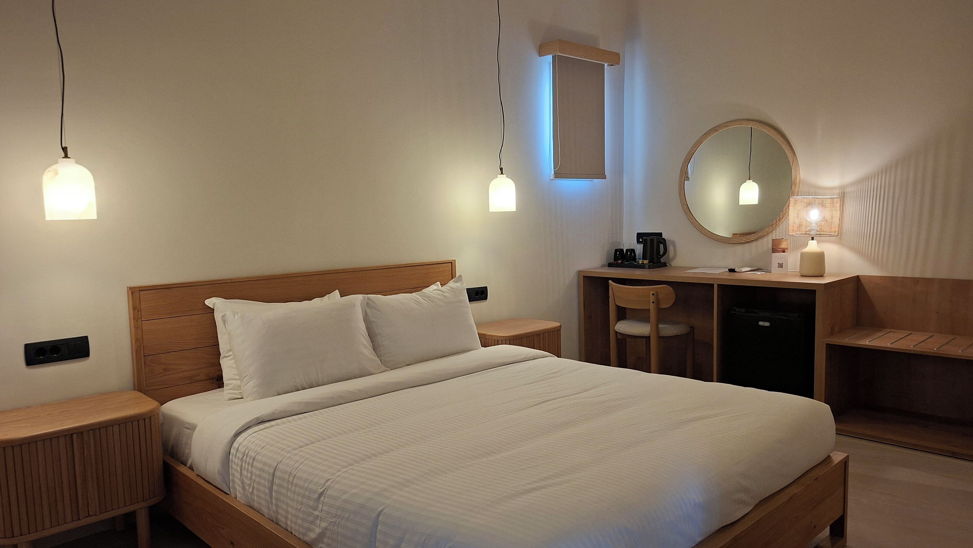 Et hotelværelse med en seng, sengeborde, et skrivebord med stol, et spejl og en lampe.